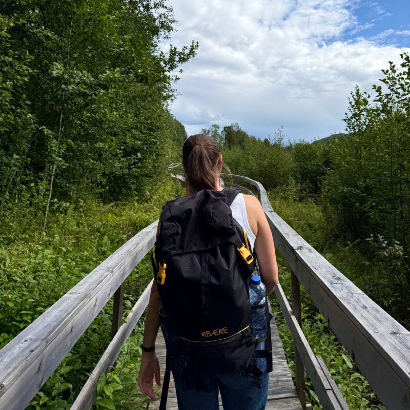 Vrouw met rugzak loopt over houten brug door natuur